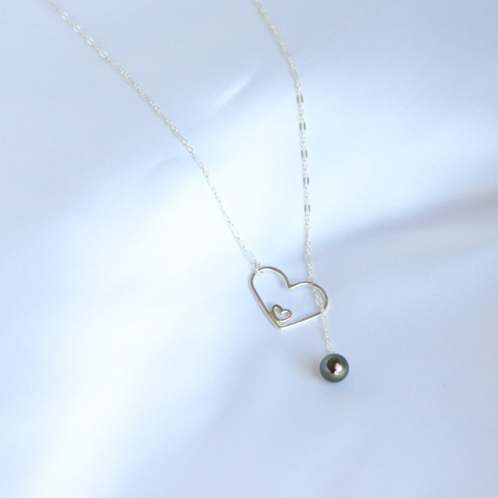 Silver necklace with a heart-shaped pendant and a tahitian pearl on a white background