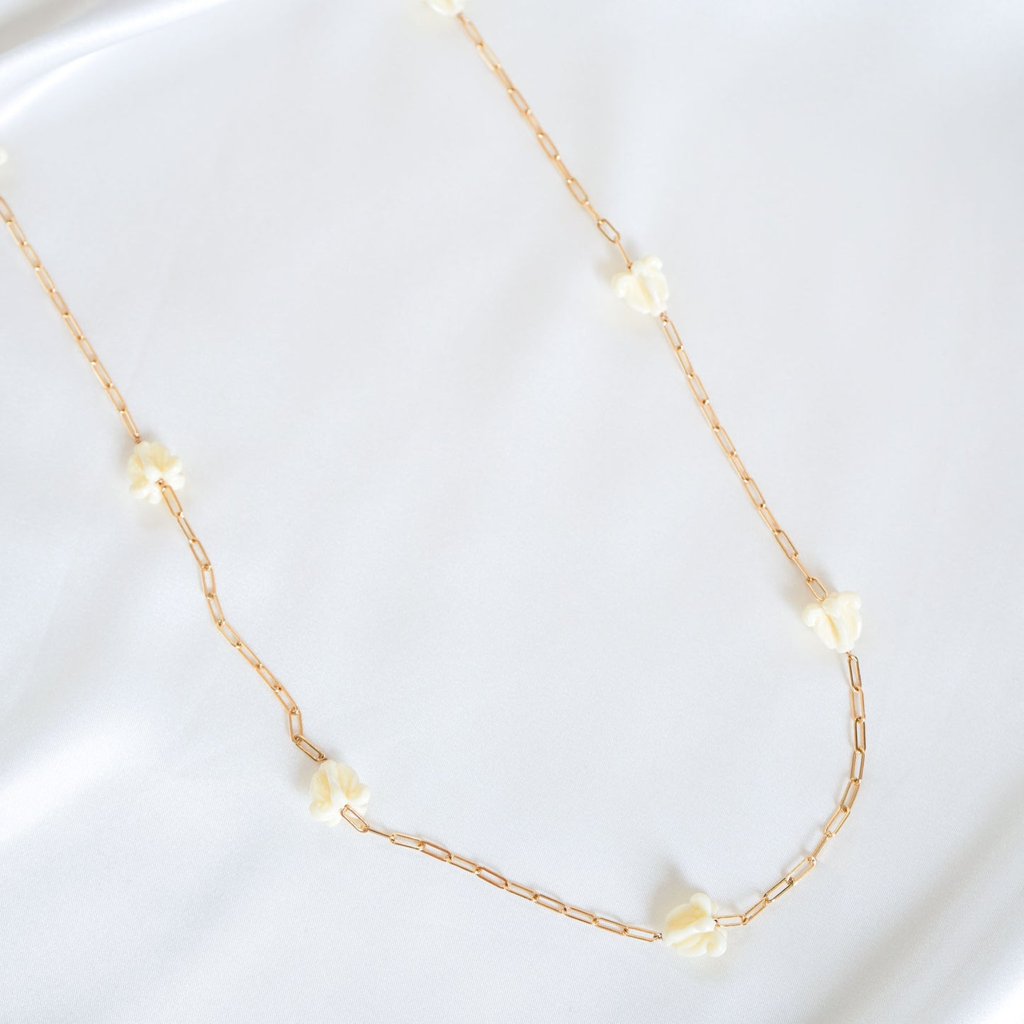 Delicate gold necklace with white crown flower beads on a white background