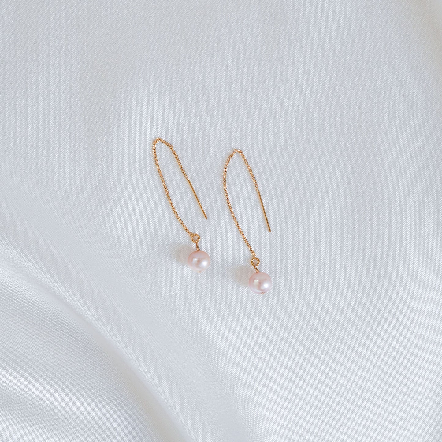 Pair of light pink pearl earrings on a white background