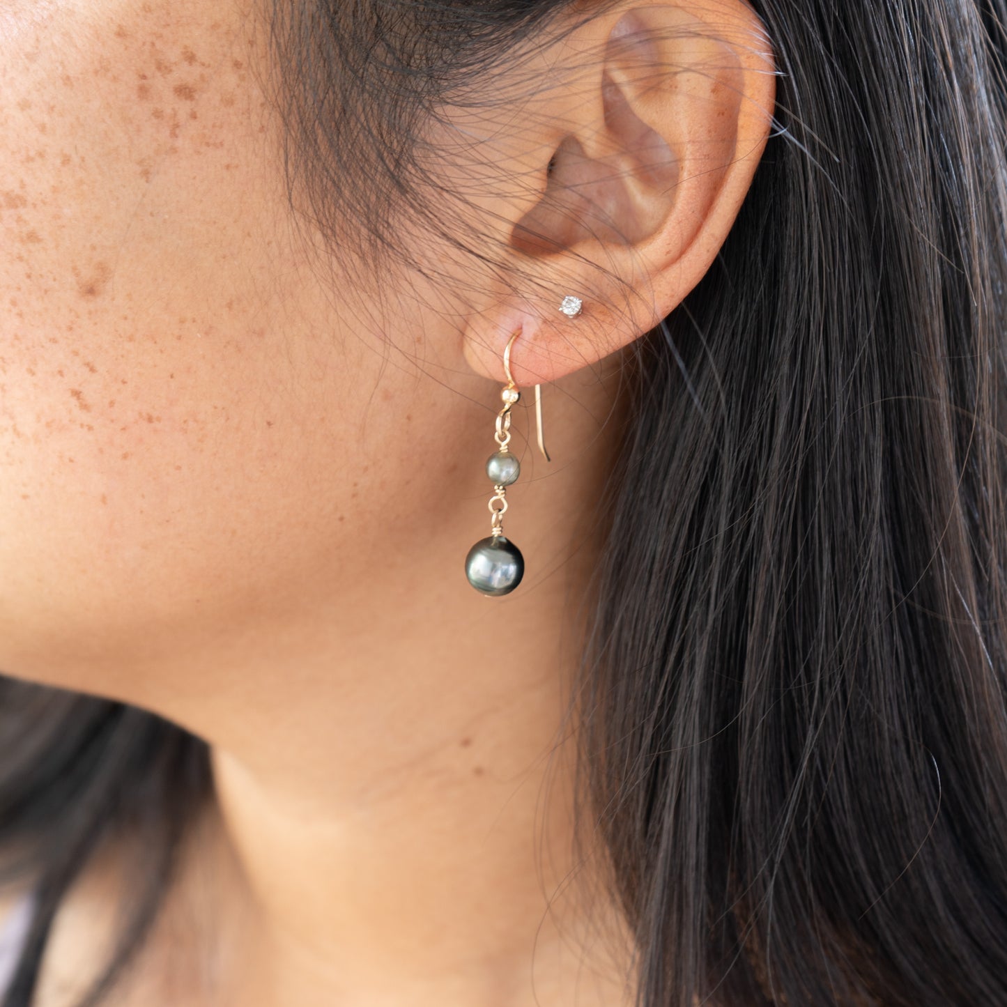 Close-up of an ear wearing a dangling double Tahitian pearl earring.