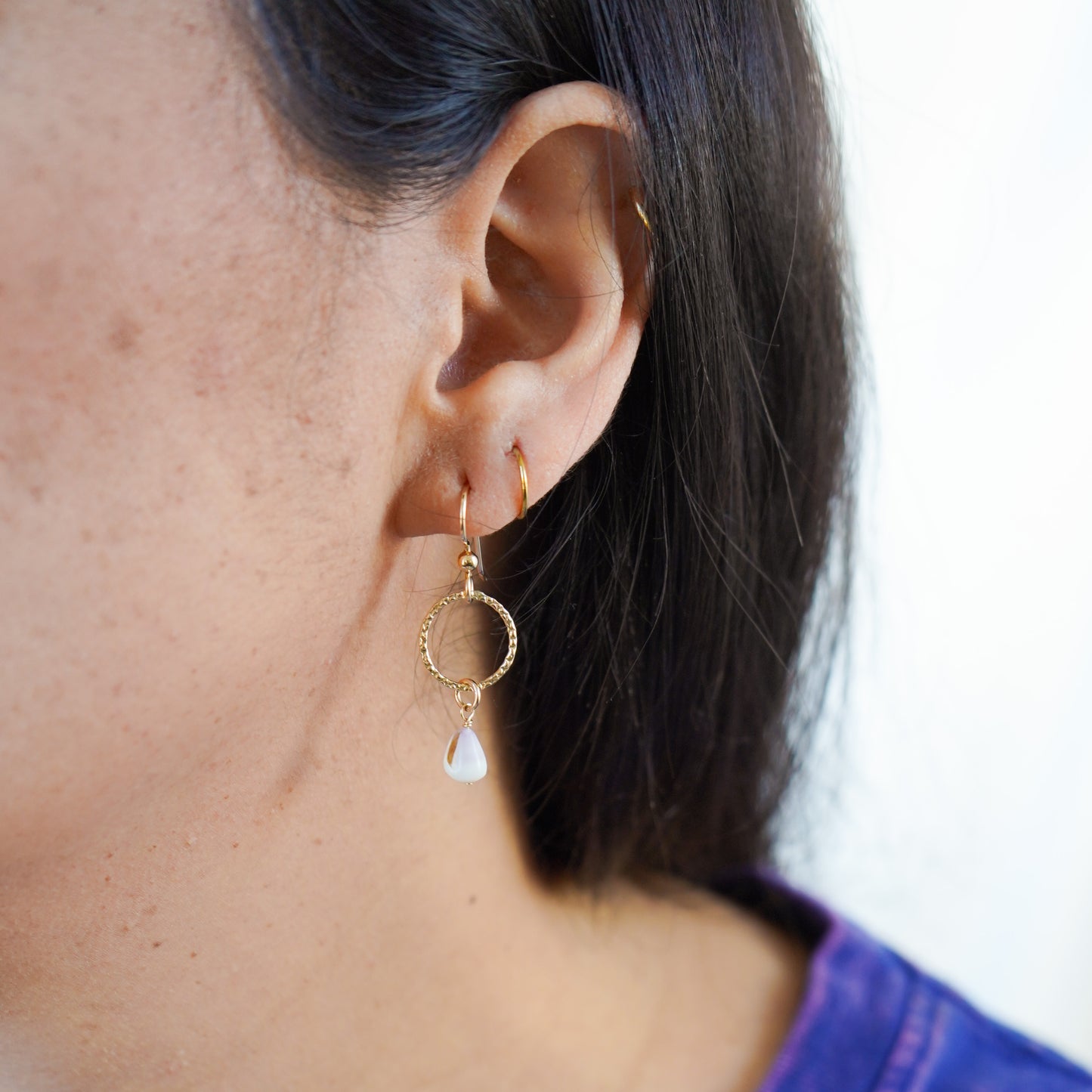 Close-up of an ear wearing gold circle dangle earrings with a tiny white cone shell.