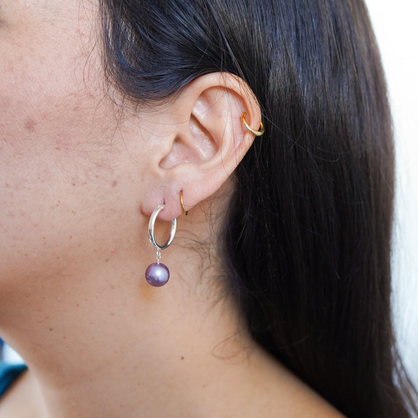 Close-up of an ear wearing silver hoop earrings with a pink edison pearl.