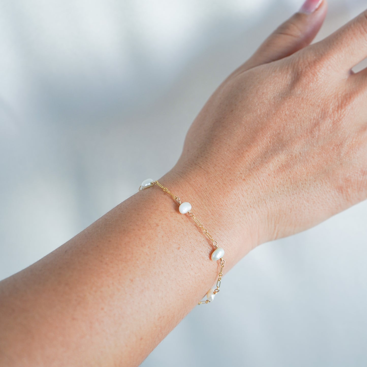 Hand wearing a delicate gold bracelet with small pearls against a blurred background