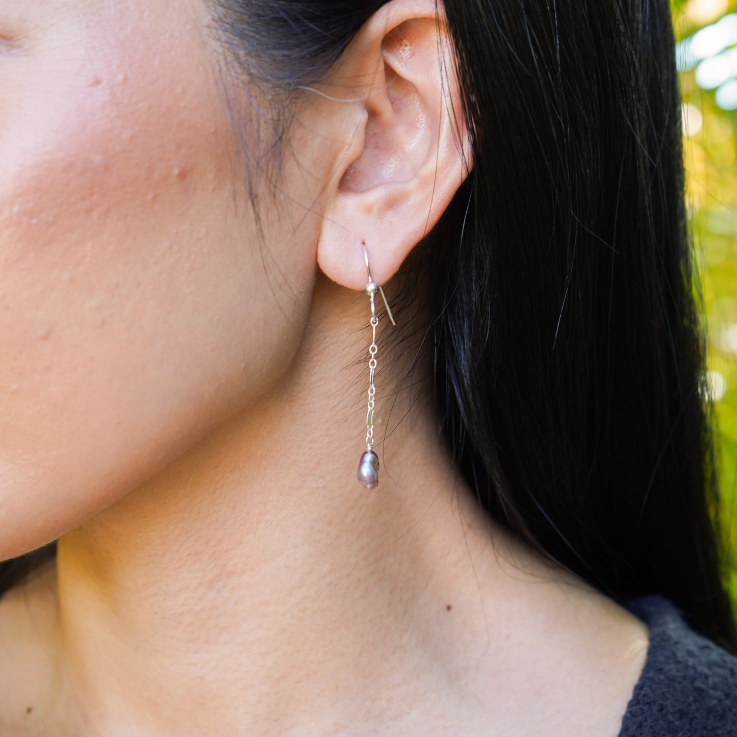 Close-up of a person wearing a dangling earring with a pearl accent.