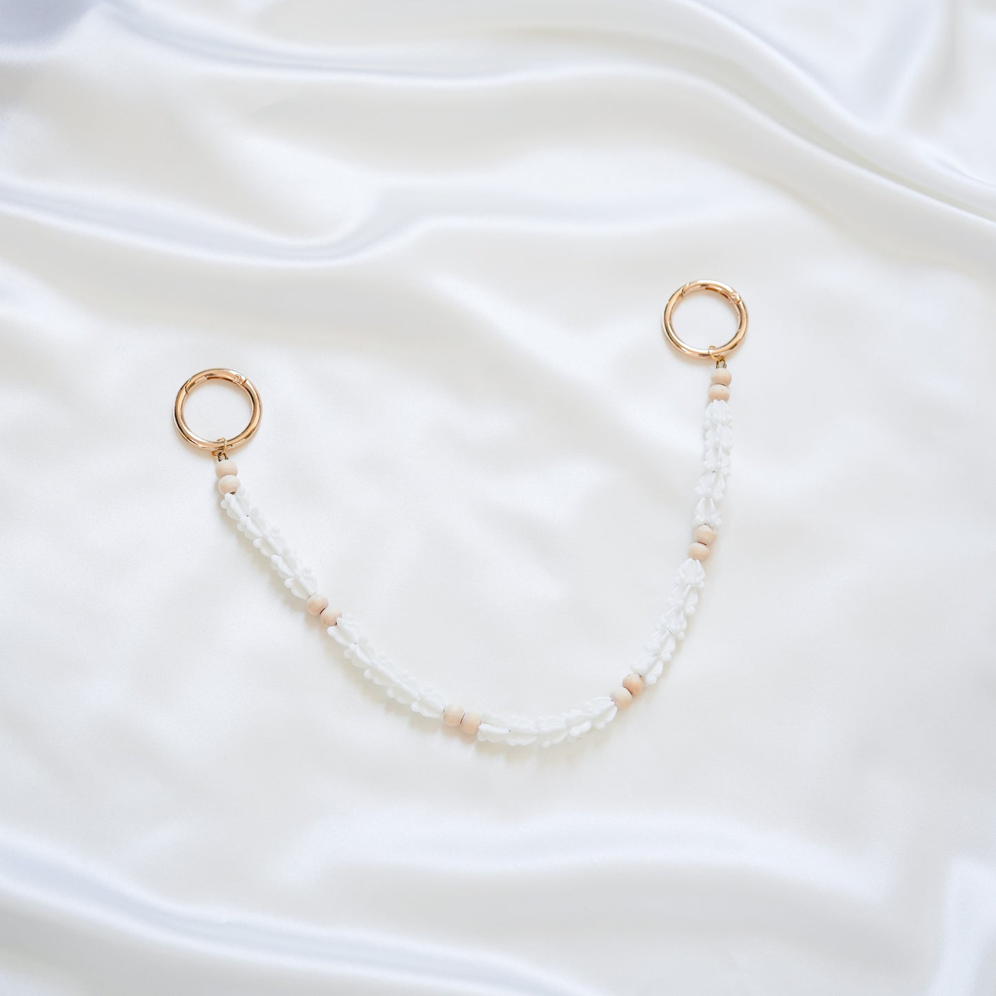 Delicate bag lei featuring white crown flower beads and light tan beads with gold rings on each end on a white fabric background