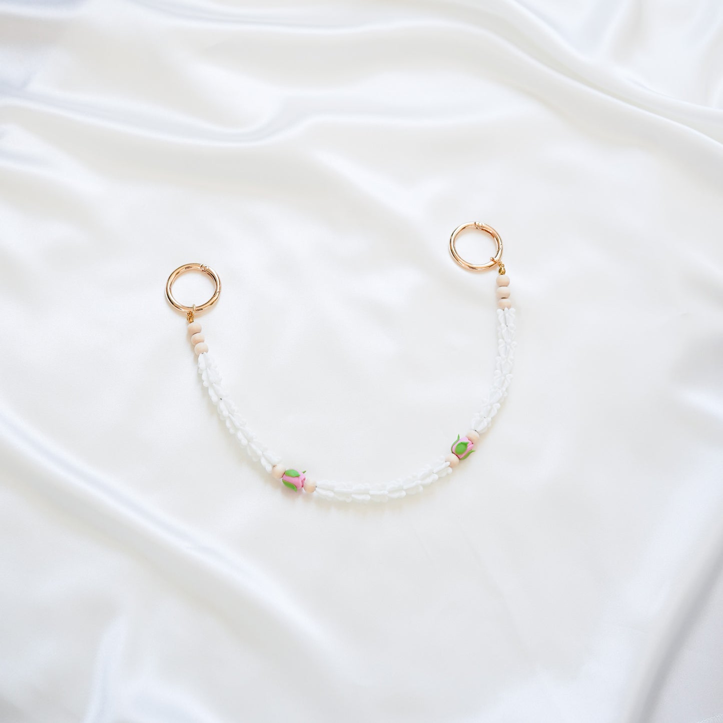 Delicate bag lei featuring white crown flower and two pink rose beads with gold rings on each end on a white fabric background