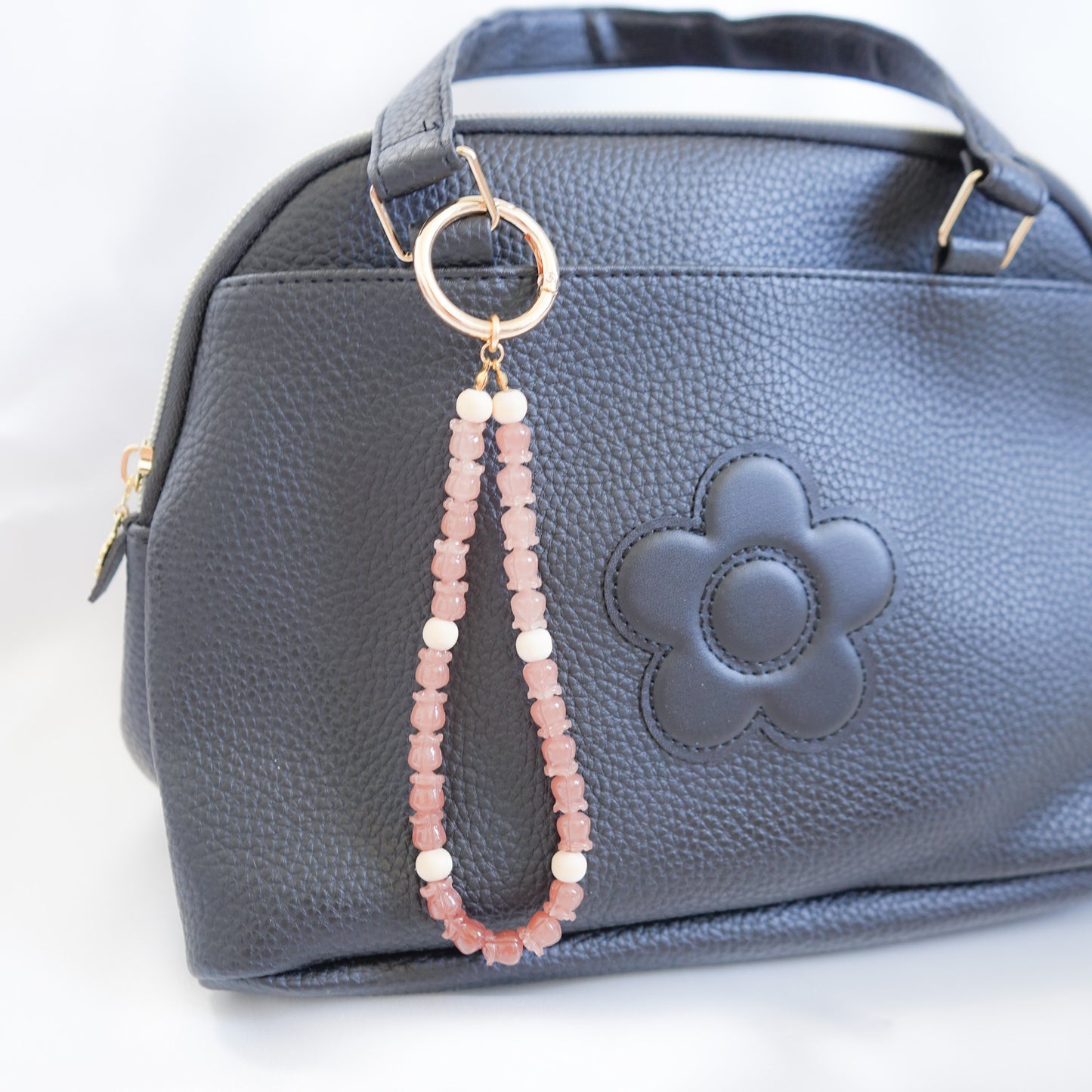 Close up of Black handbag with a floral design and a beaded strap on a white background