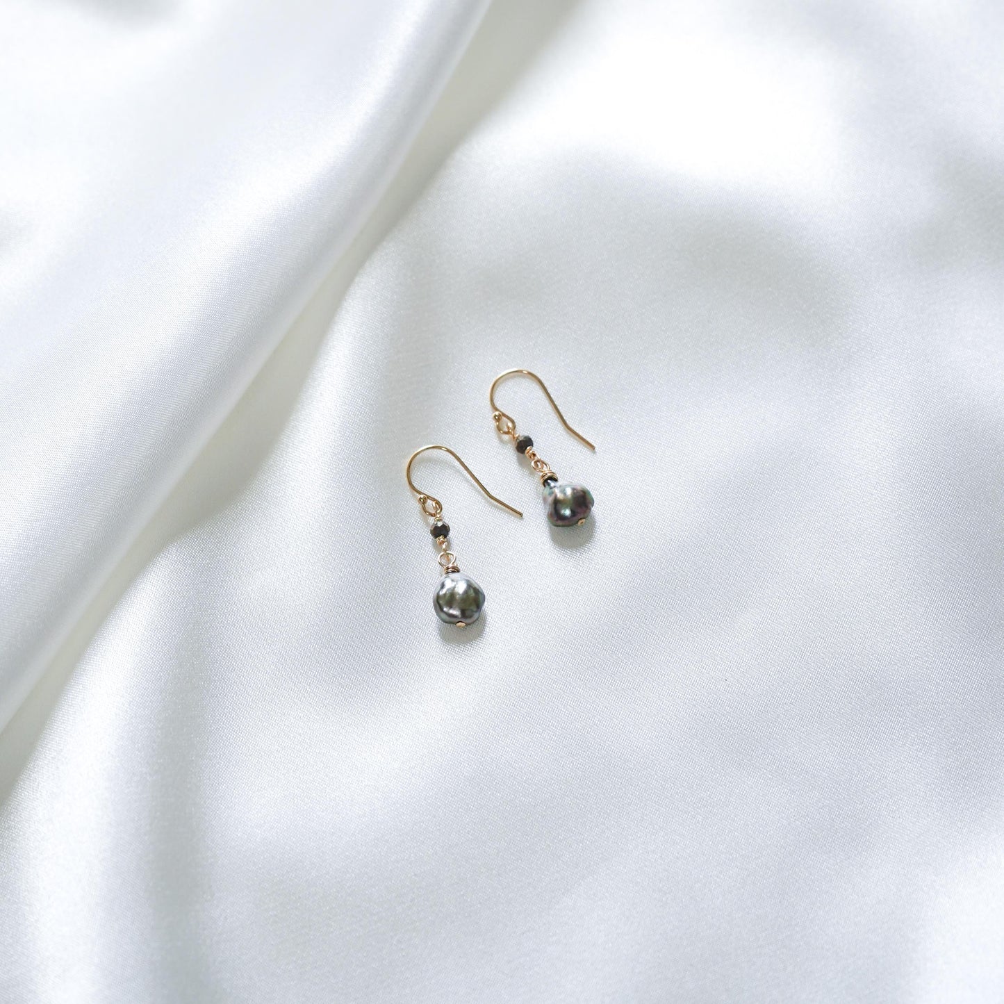 Pair of pearl earrings with black spinel bead on a white fabric background