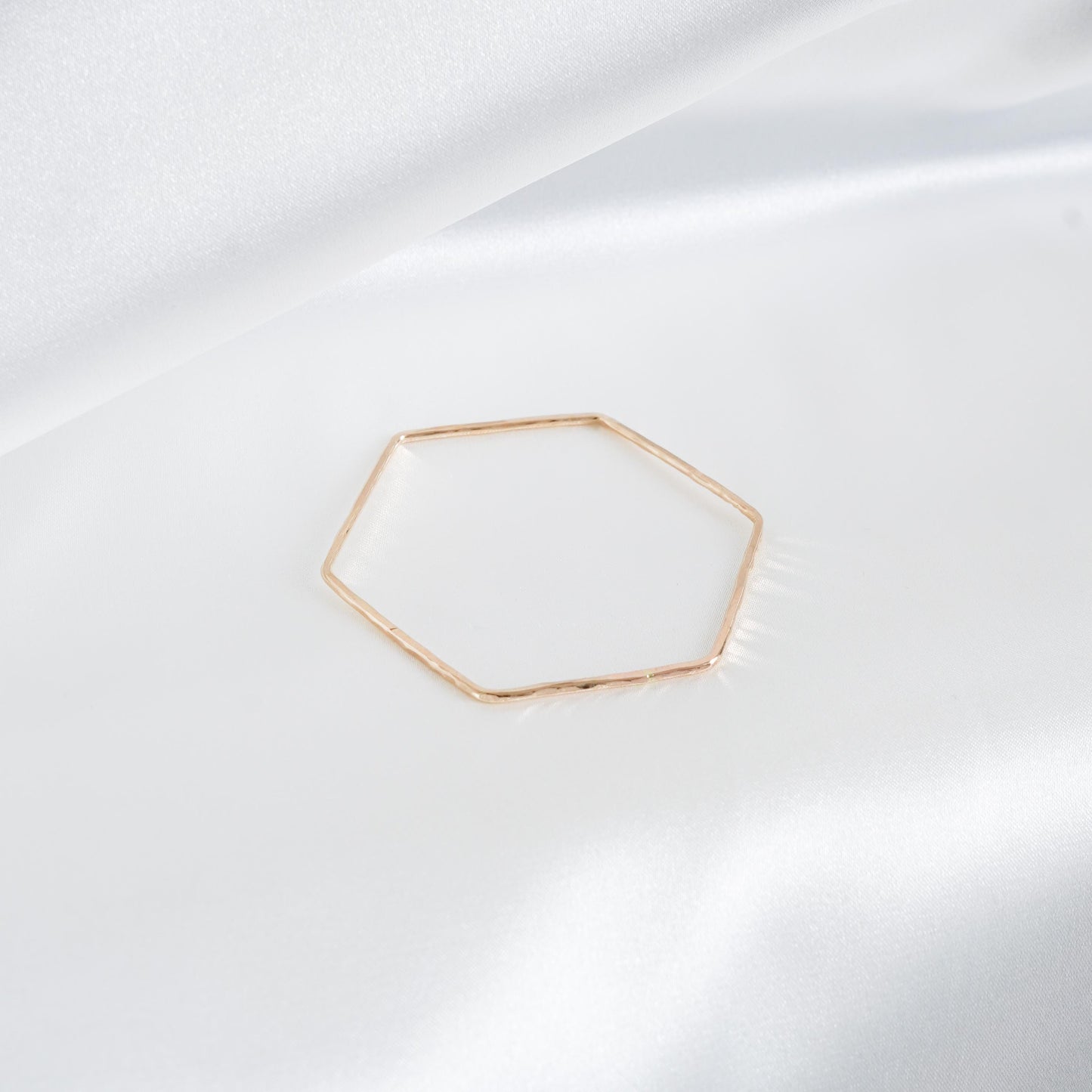 Gold hexagonal bangle on a white fabric background