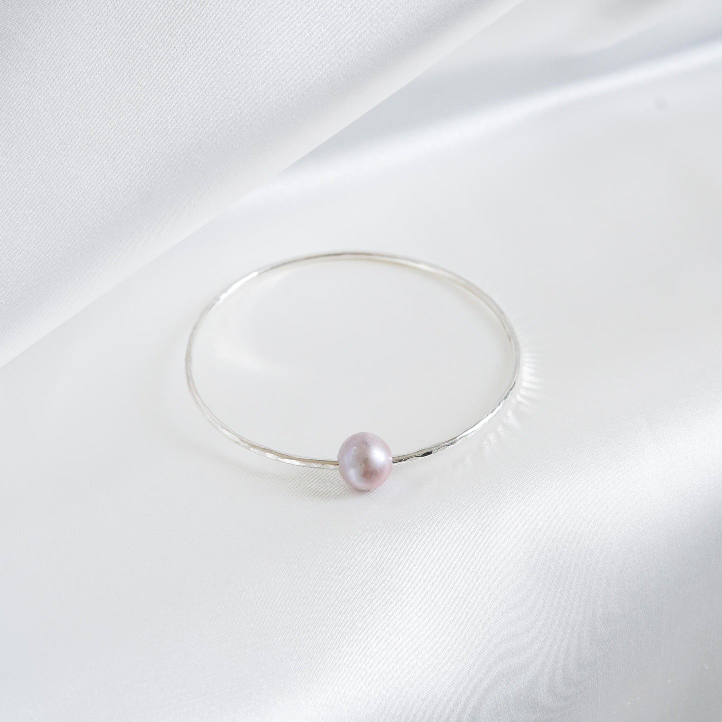 Silver bracelet with a single pearl on a white background