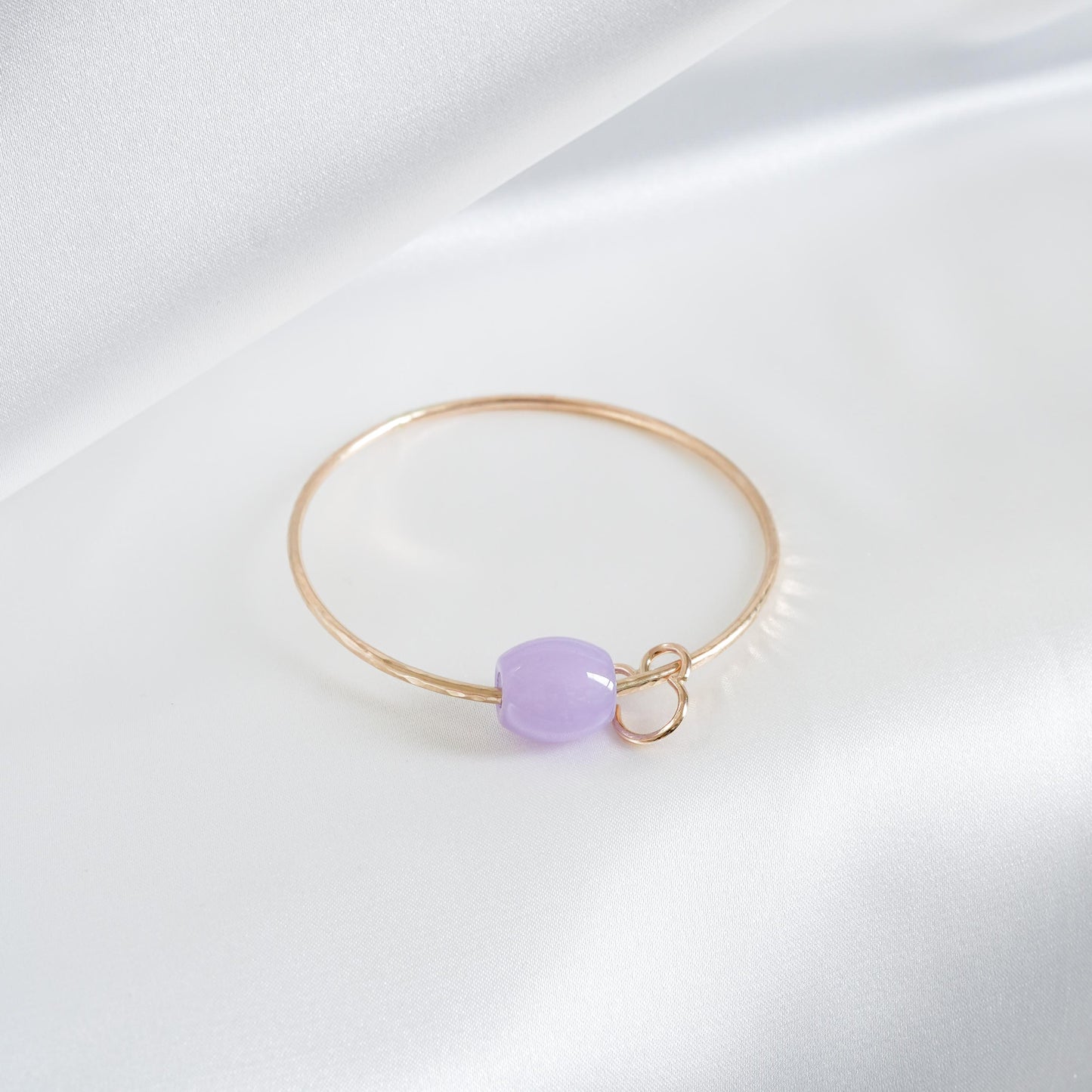 Gold bracelet with a purple jade bead and mickey mouse charm on a white background