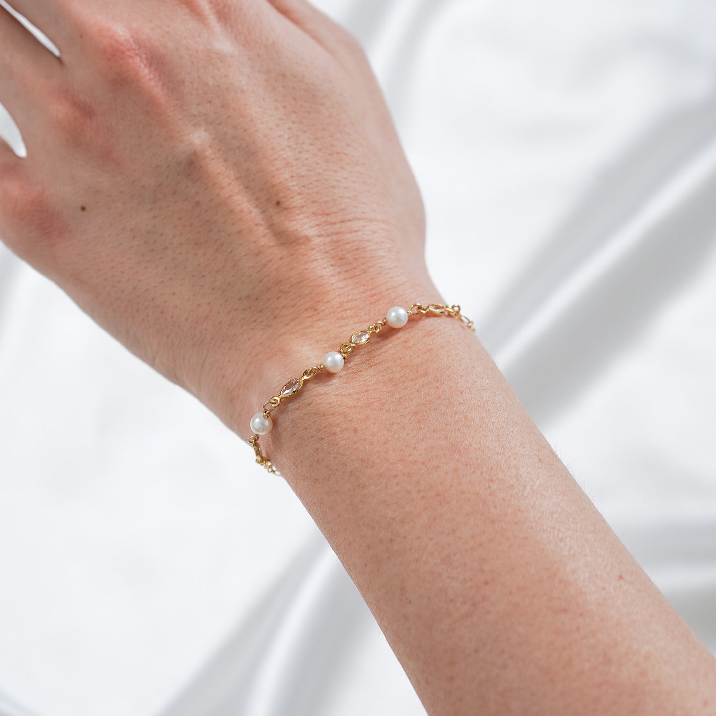 Gold bracelet with white pearls and cz stones on a wrist against white background