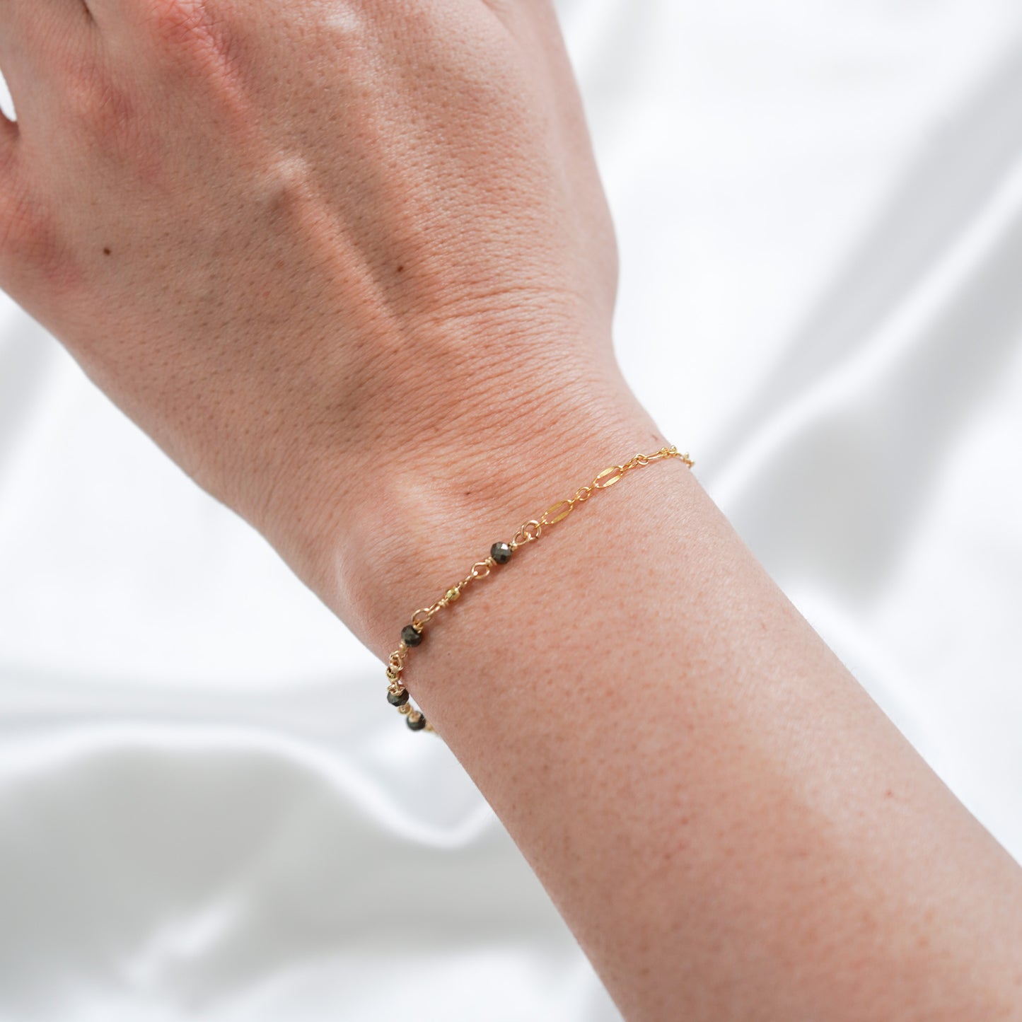 Gold necklace with black stones on a wrist against white background