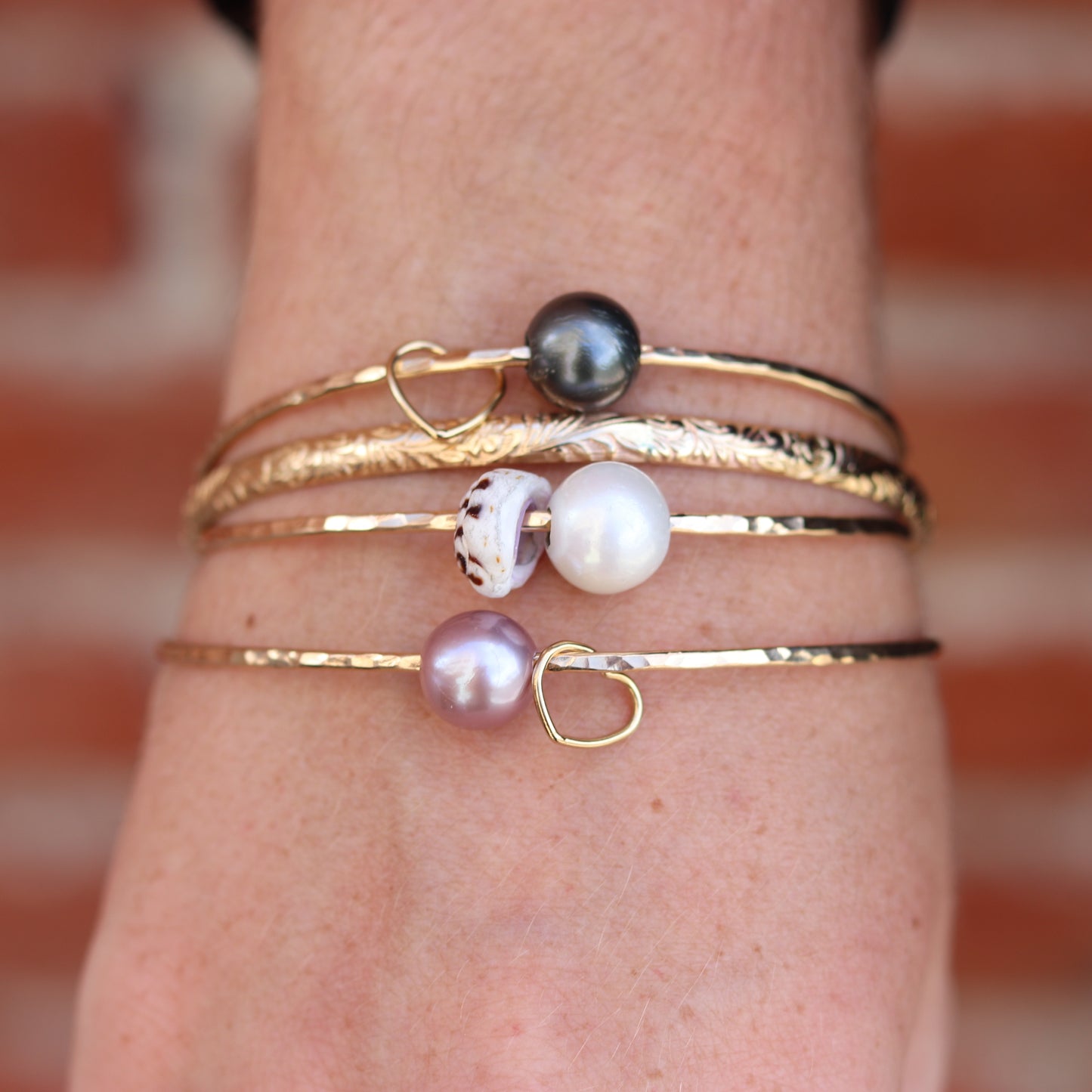 Close-up of a wrist wearing multiple gold bracelets with pearls and charms against a blurred background