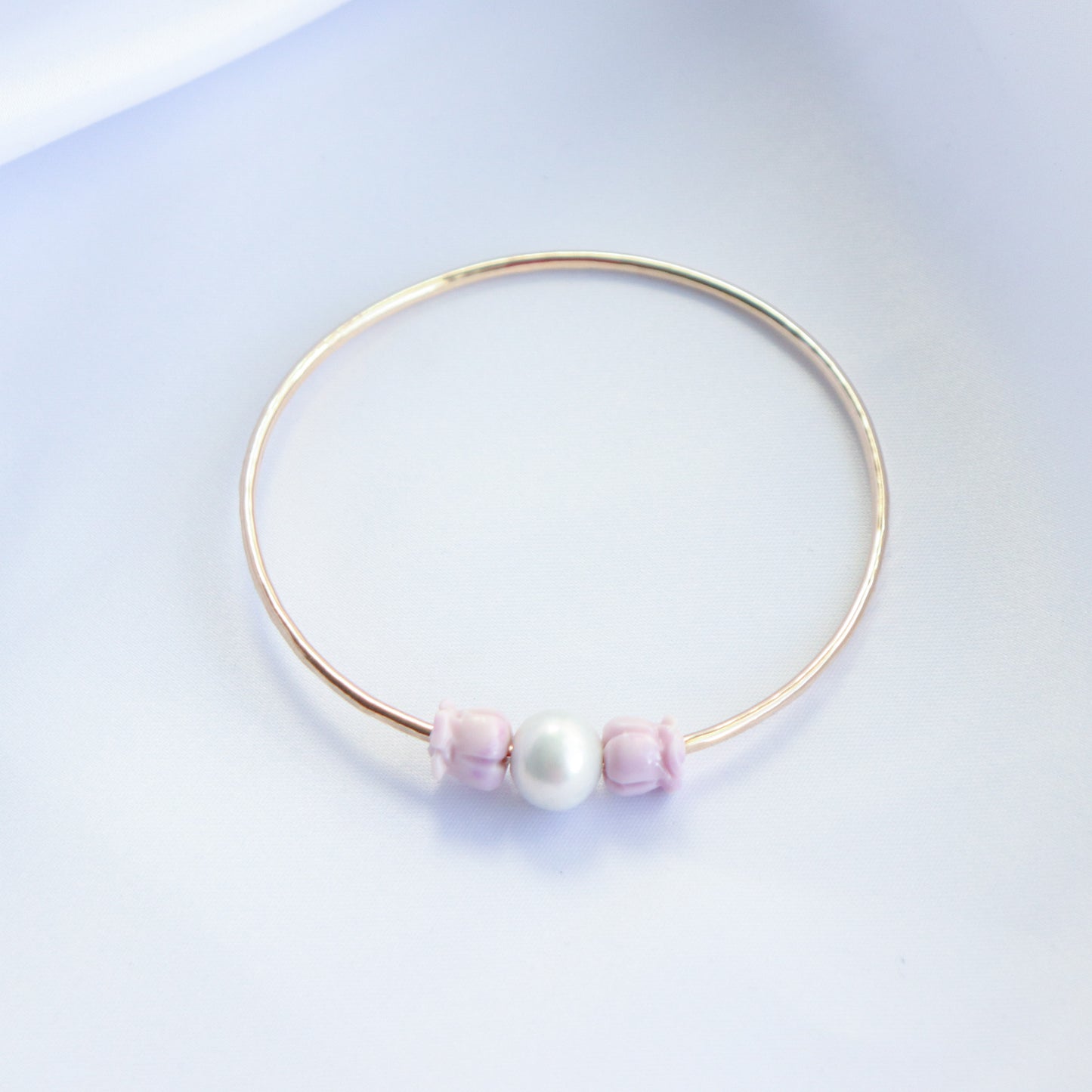 Gold bracelet with a white pearl and lavender rose bead on both sides of pearl on a white background