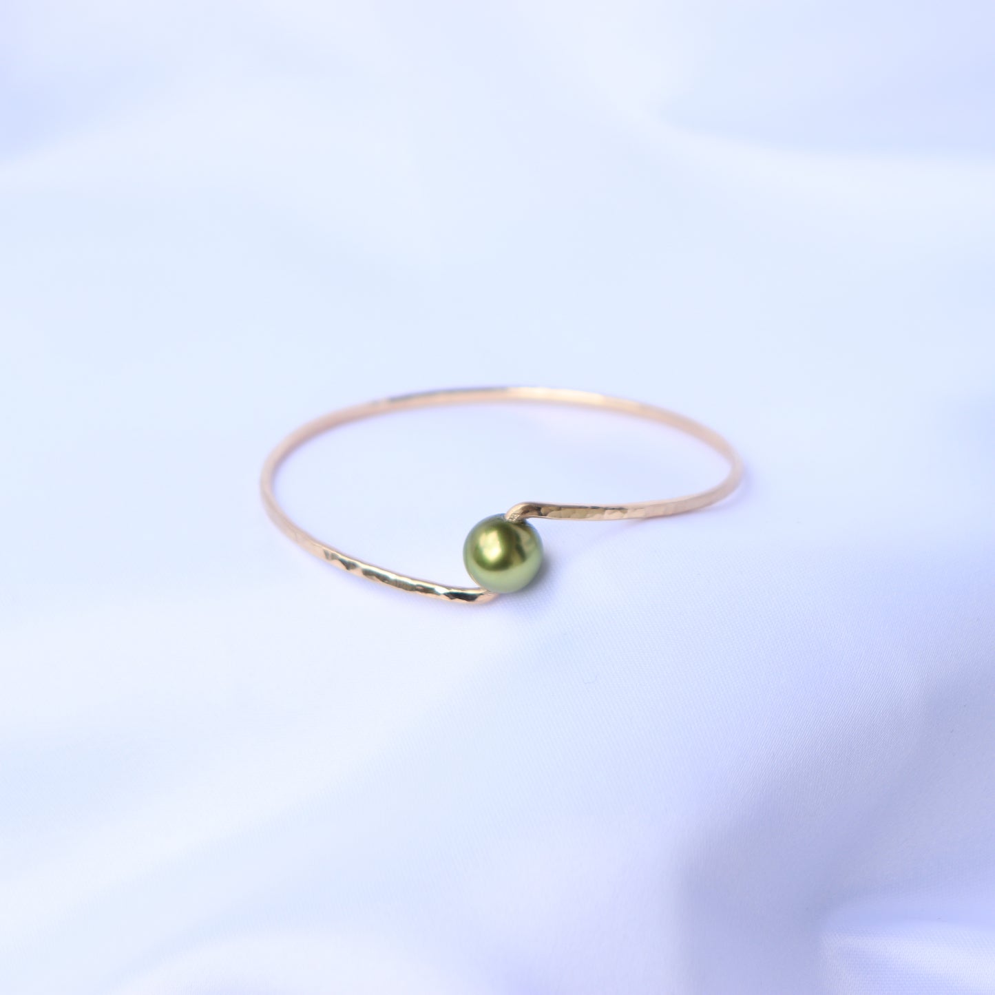 Gold bracelet with a green pearl on a white background