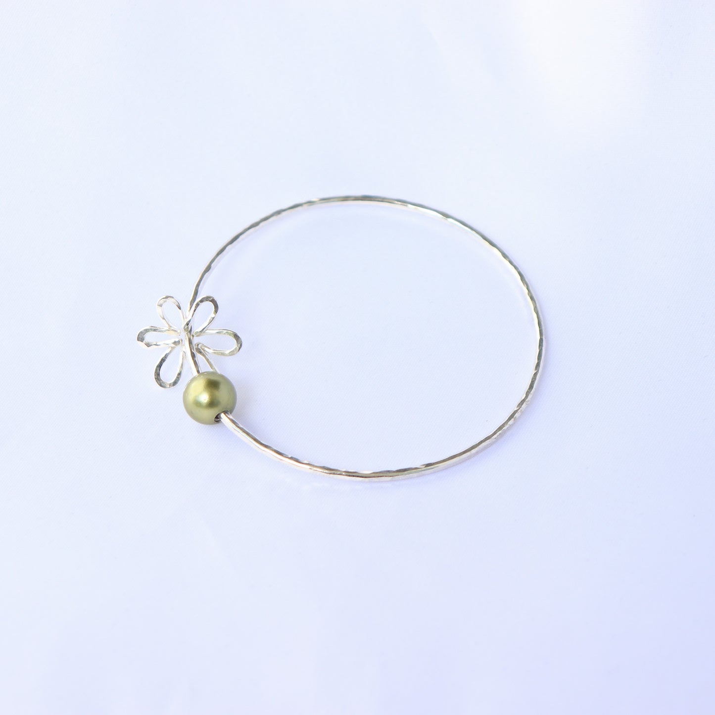 Gold bracelet with a green pearl and flower charm on a white background