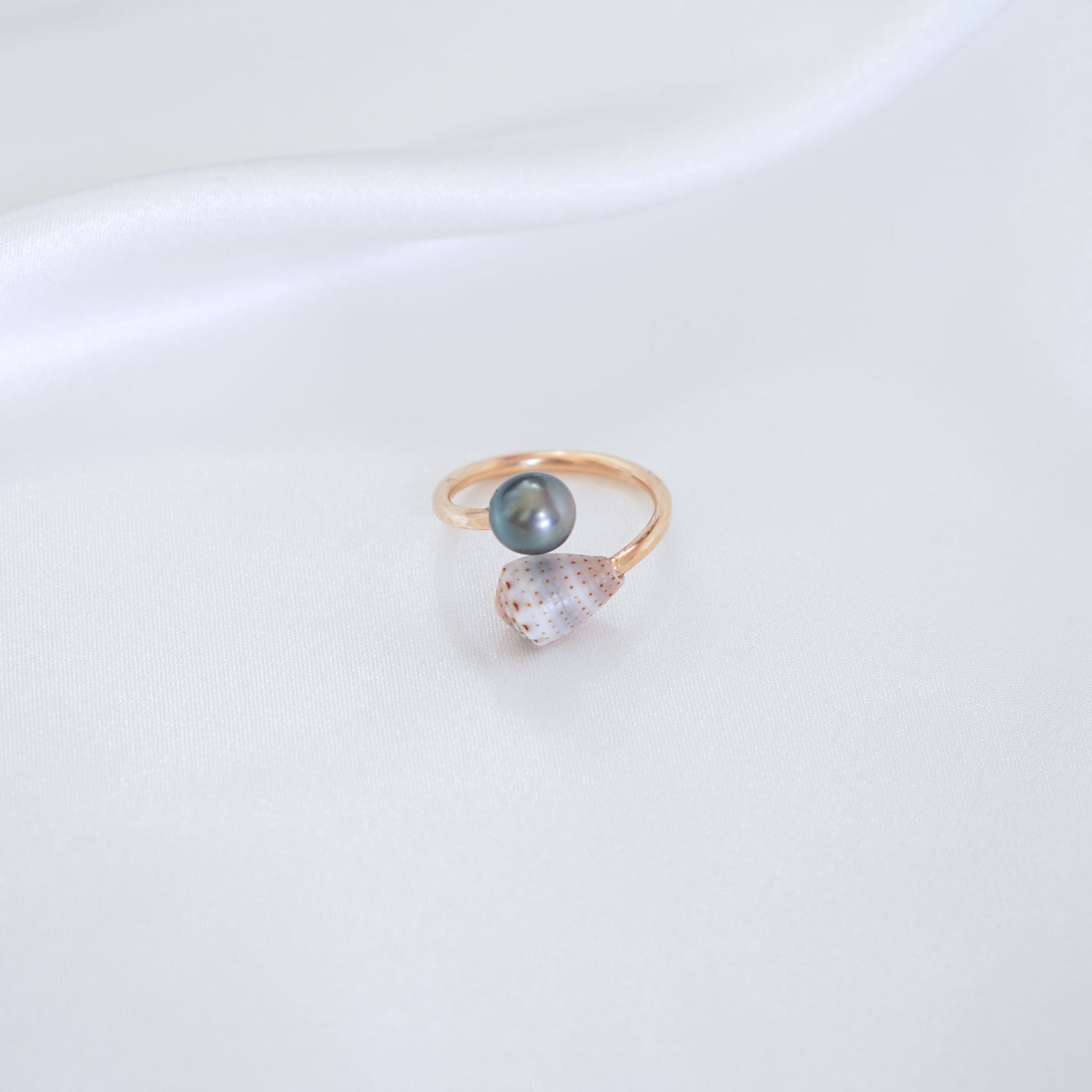 Gold ring with a tahitian pearl and patterned cone shell on a white background