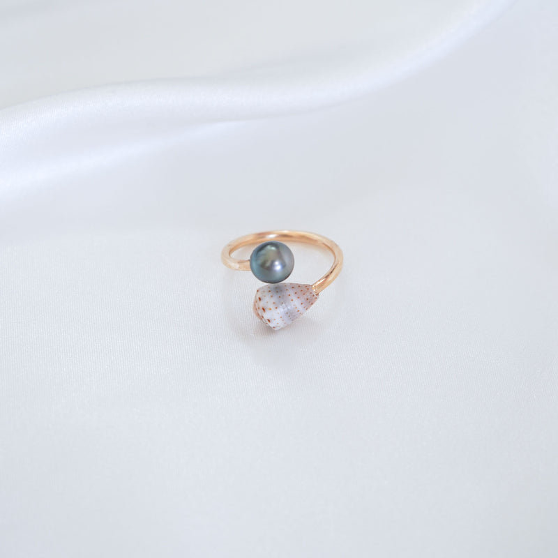 Gold ring with a tahitian pearl and patterned cone shell on a white background
