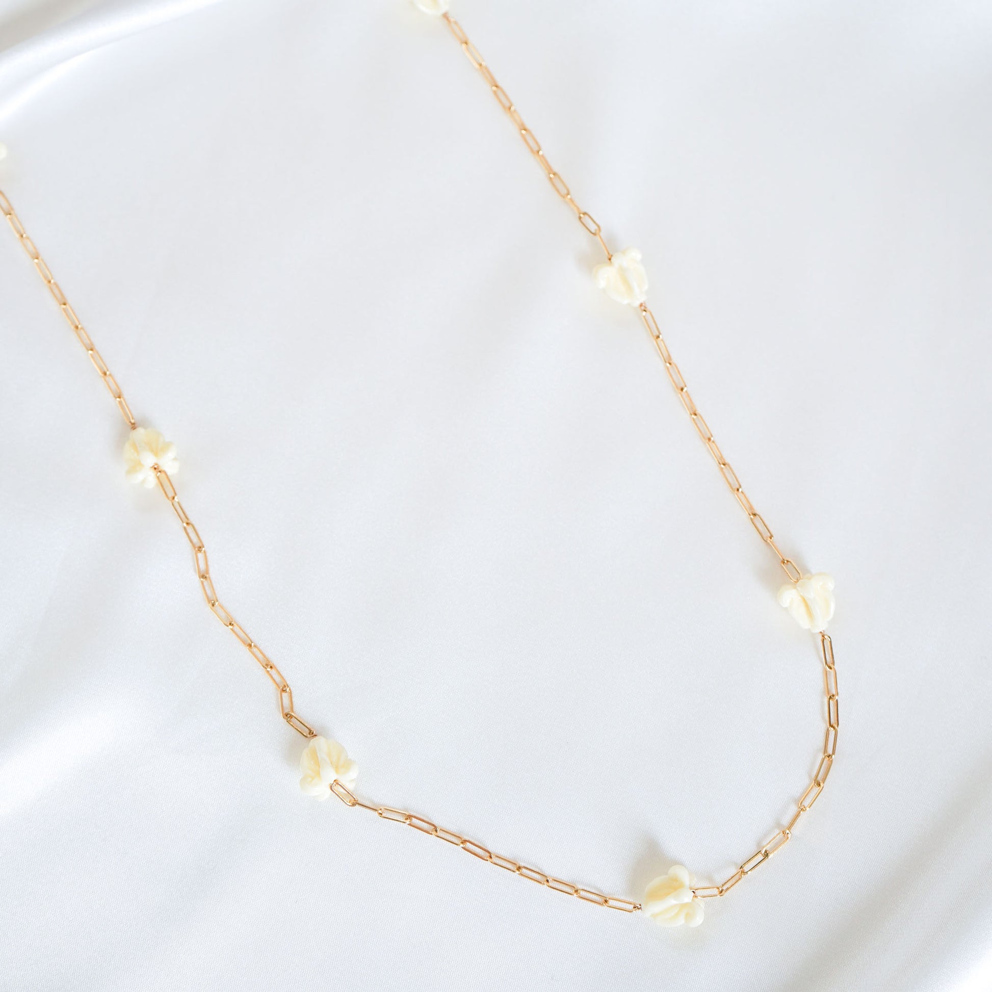 Delicate gold necklace with white crown flower beads on a white background