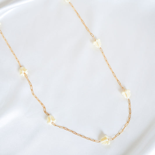 Delicate gold necklace with white crown flower beads on a white background