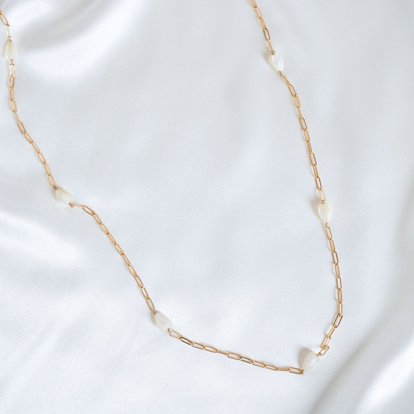 Gold chain necklace with white pikake beads on a white background