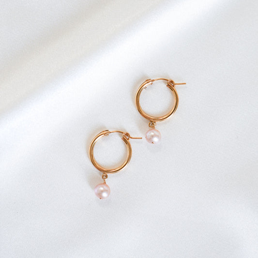 Gold hoop earrings with pink pearls on a white background