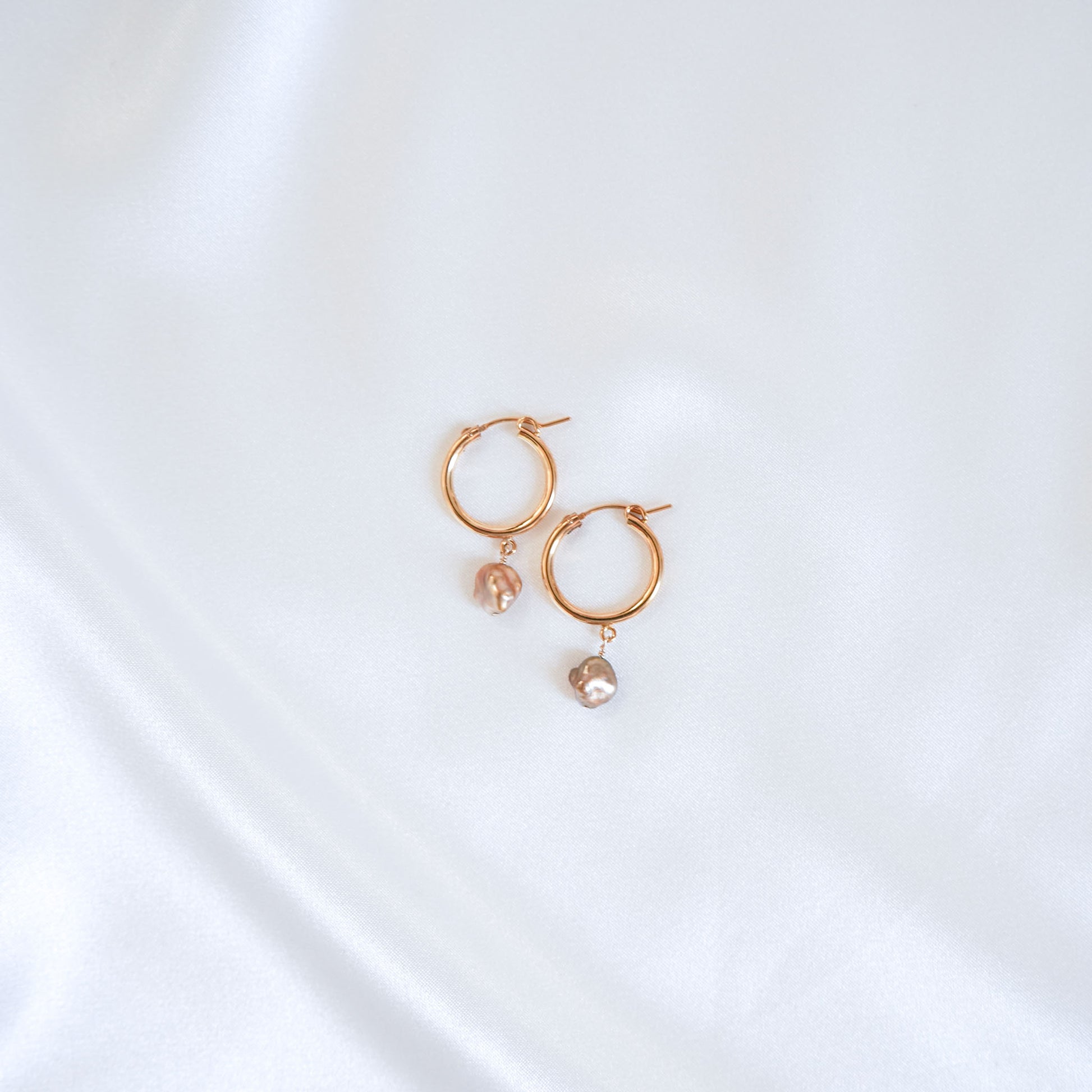 Gold hoop earrings with pearl drops on a white background