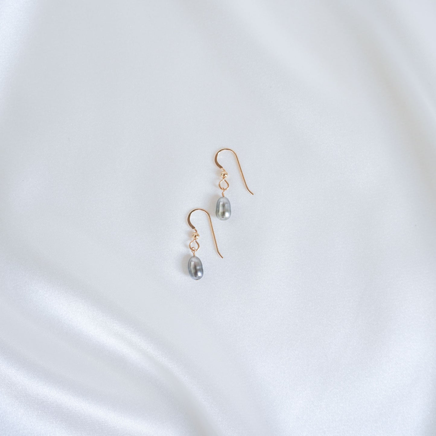 Gold earrings with pearl drops on a white satin background