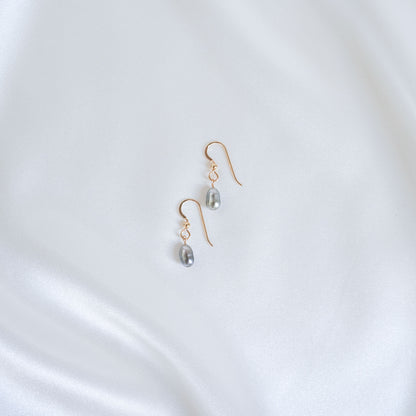 Gold earrings with pearl drops on a white satin background