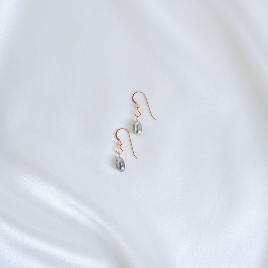 Gold earrings with pearl drops on a white satin background