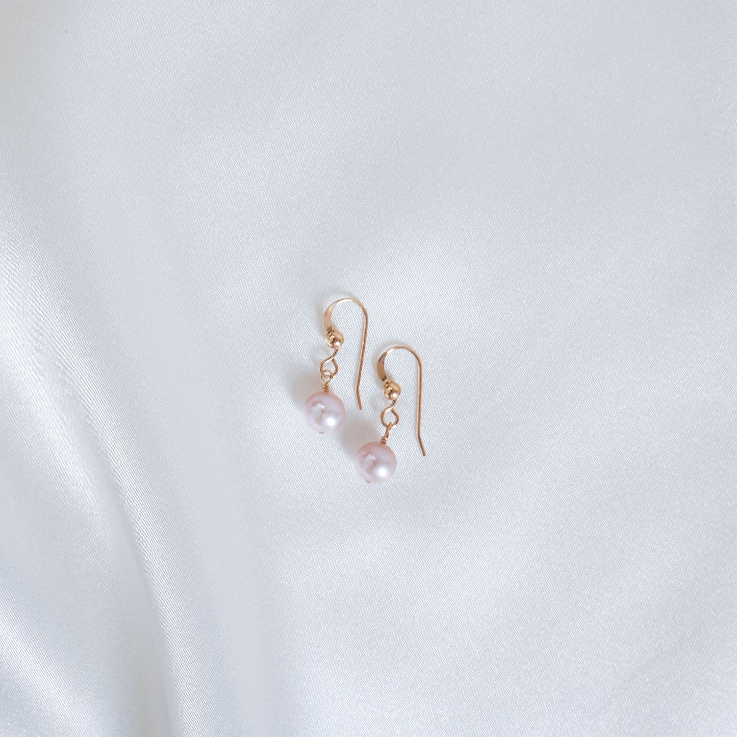Pair of pink pearl earrings on a white fabric background