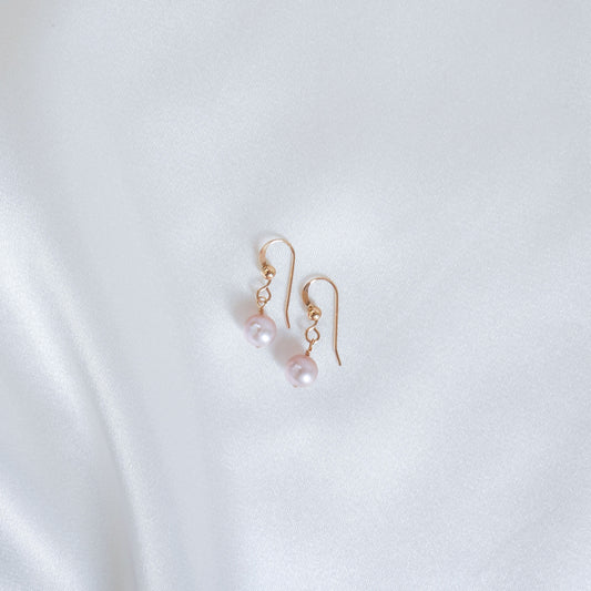 Pair of pink pearl earrings on a white fabric background