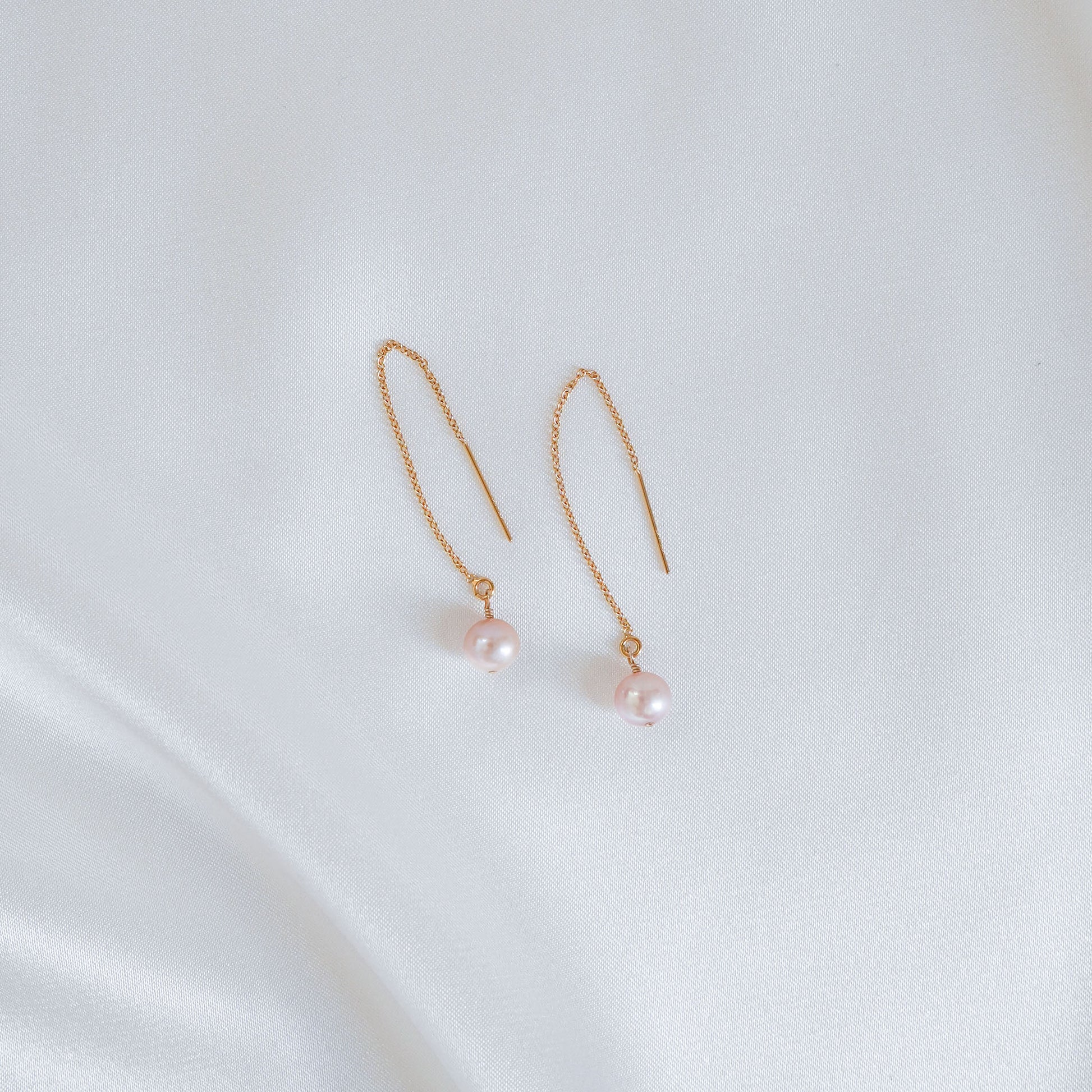 Pair of light pink pearl earrings on a white background