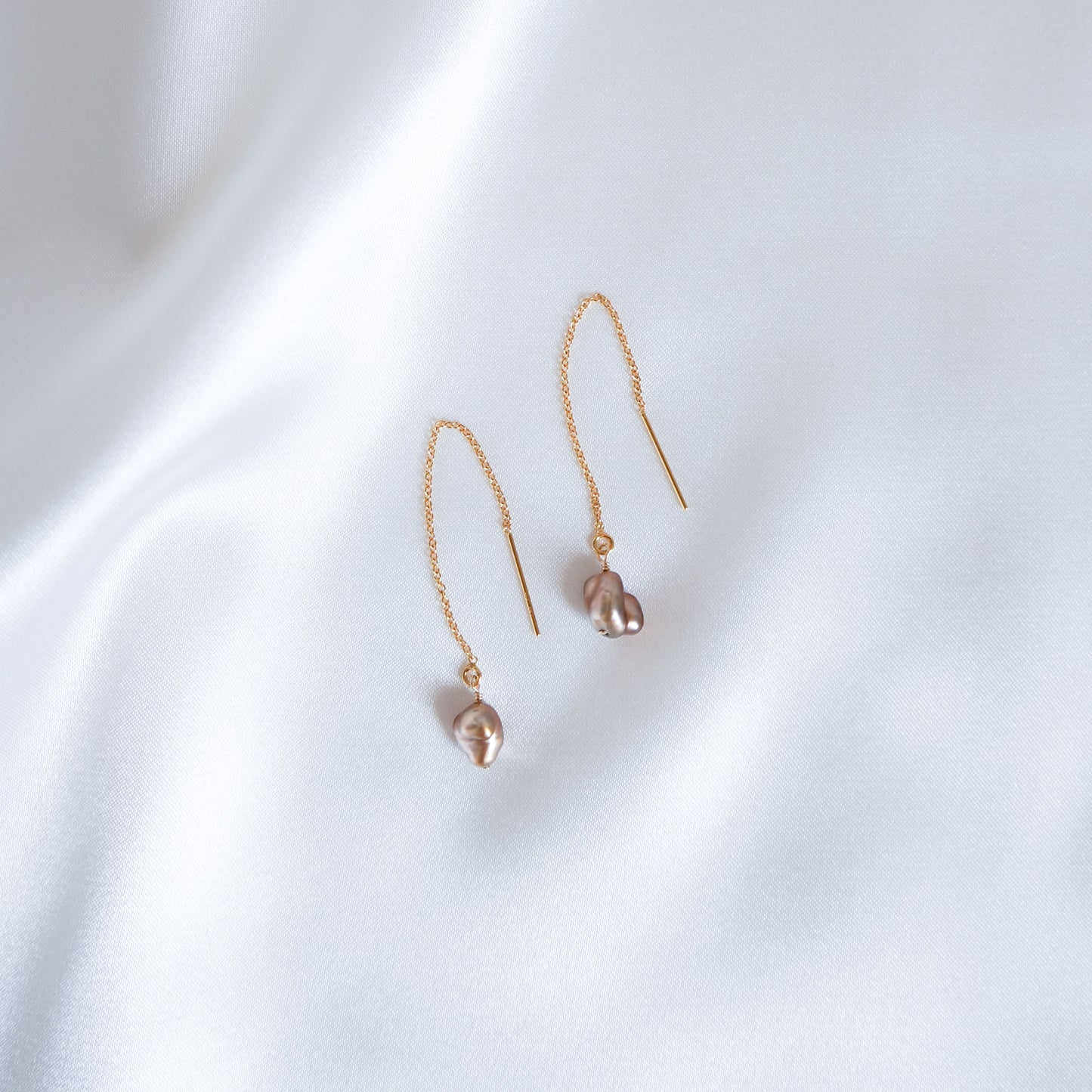 Pair of gold earrings with small brown keshi beads on a white background