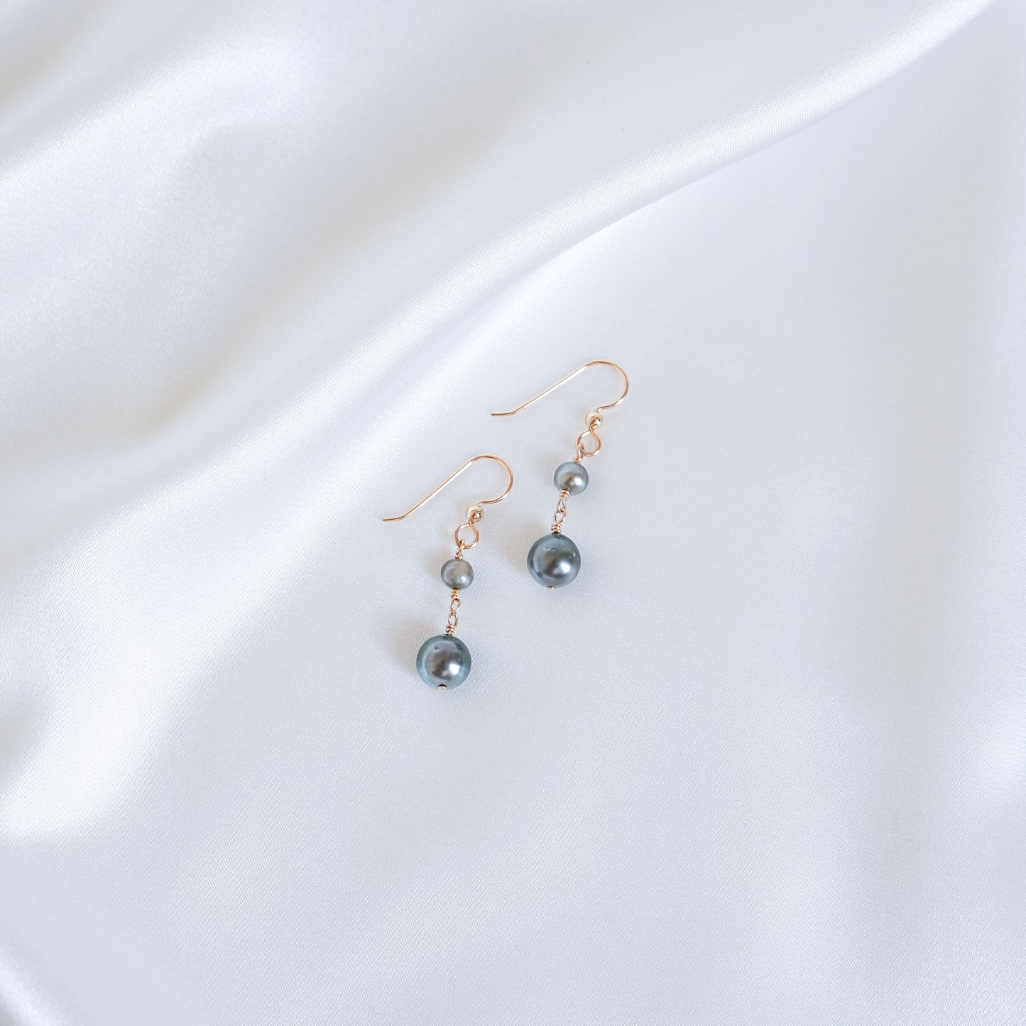 Pair of double tahitian pearl earrings on a white fabric background