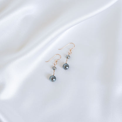 Pair of double tahitian pearl earrings on a white fabric background