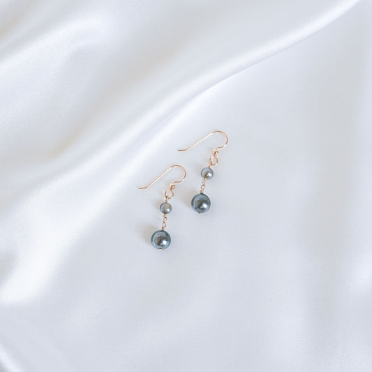 Pair of double tahitian pearl earrings on a white fabric background