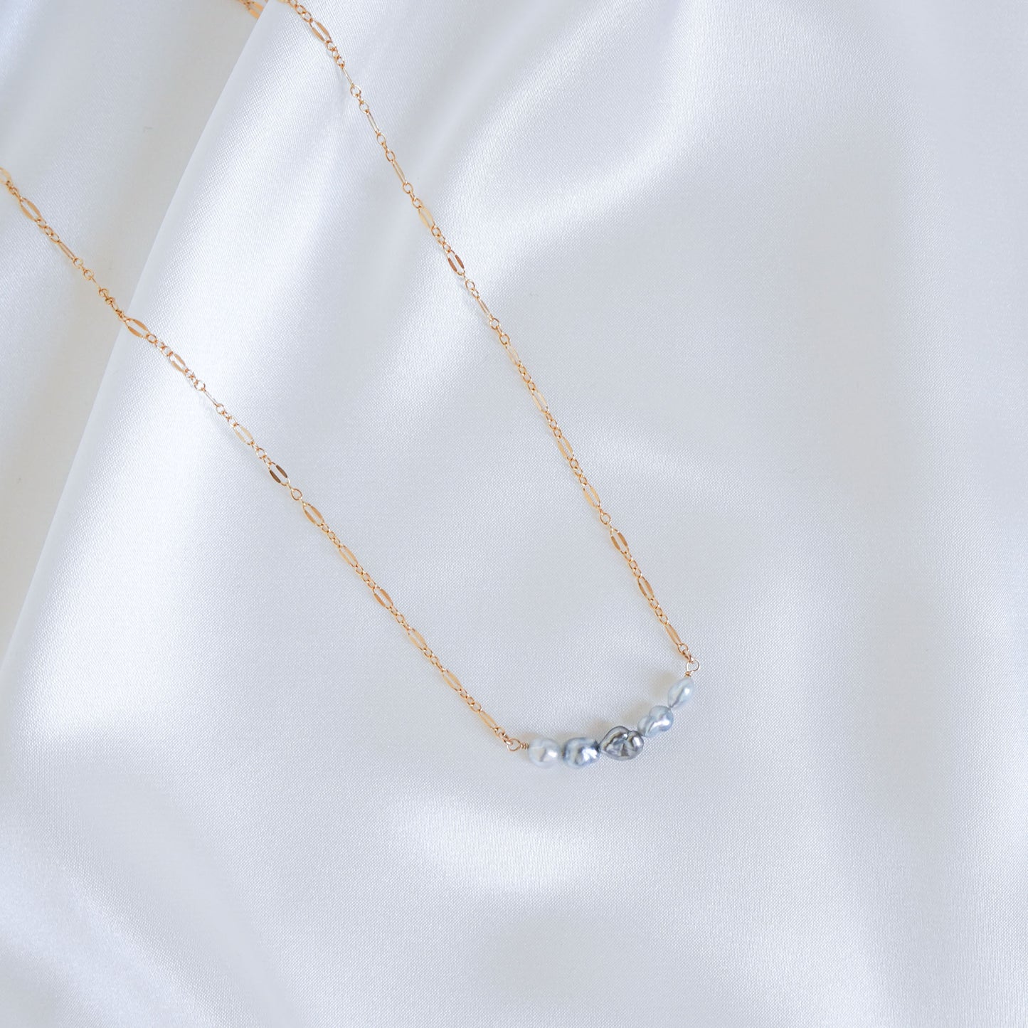Delicate gold necklace with five small blue pearls on a white fabric background