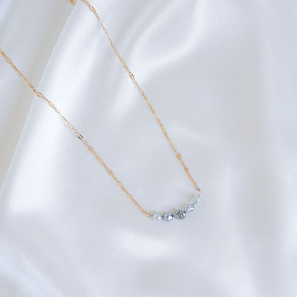 Delicate gold necklace with five small blue pearls on a white fabric background