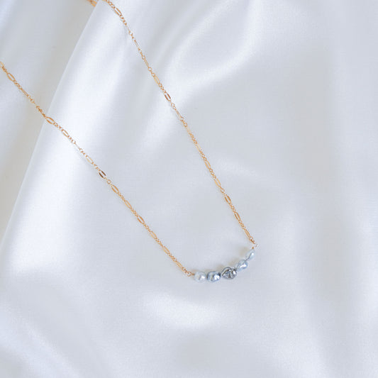 Delicate gold necklace with five small blue pearls on a white fabric background