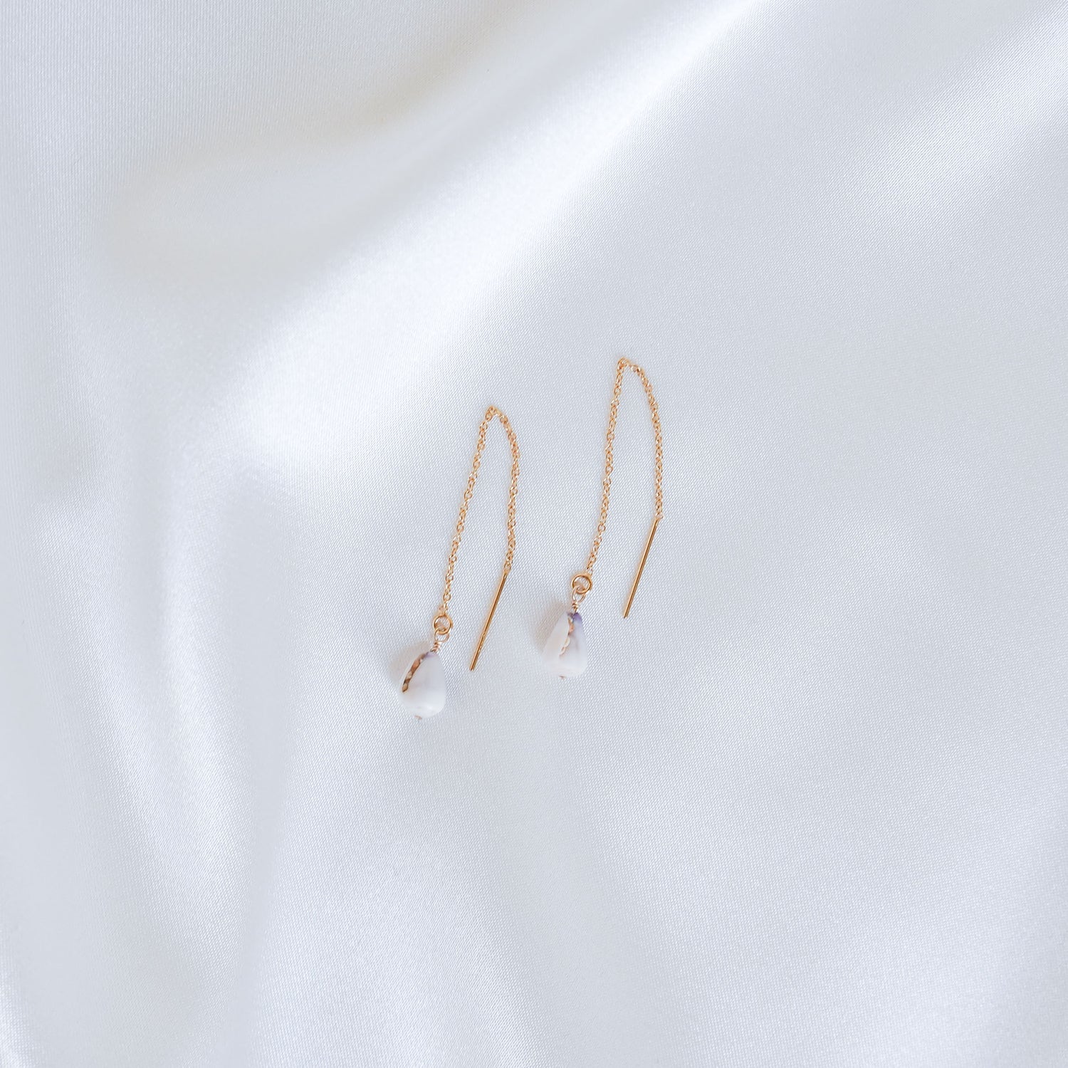 Pair of gold chain earrings with tiny cone shells on a white background