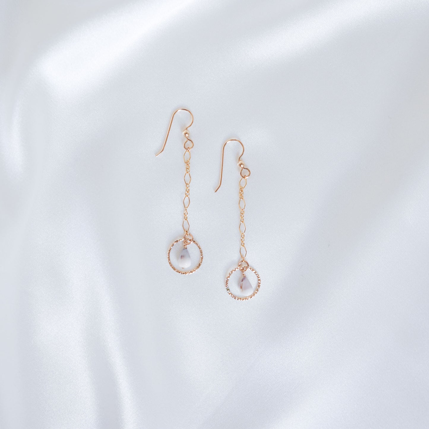 Gold dangle chain earrings with small gold circle and tiny cone shell on a white background