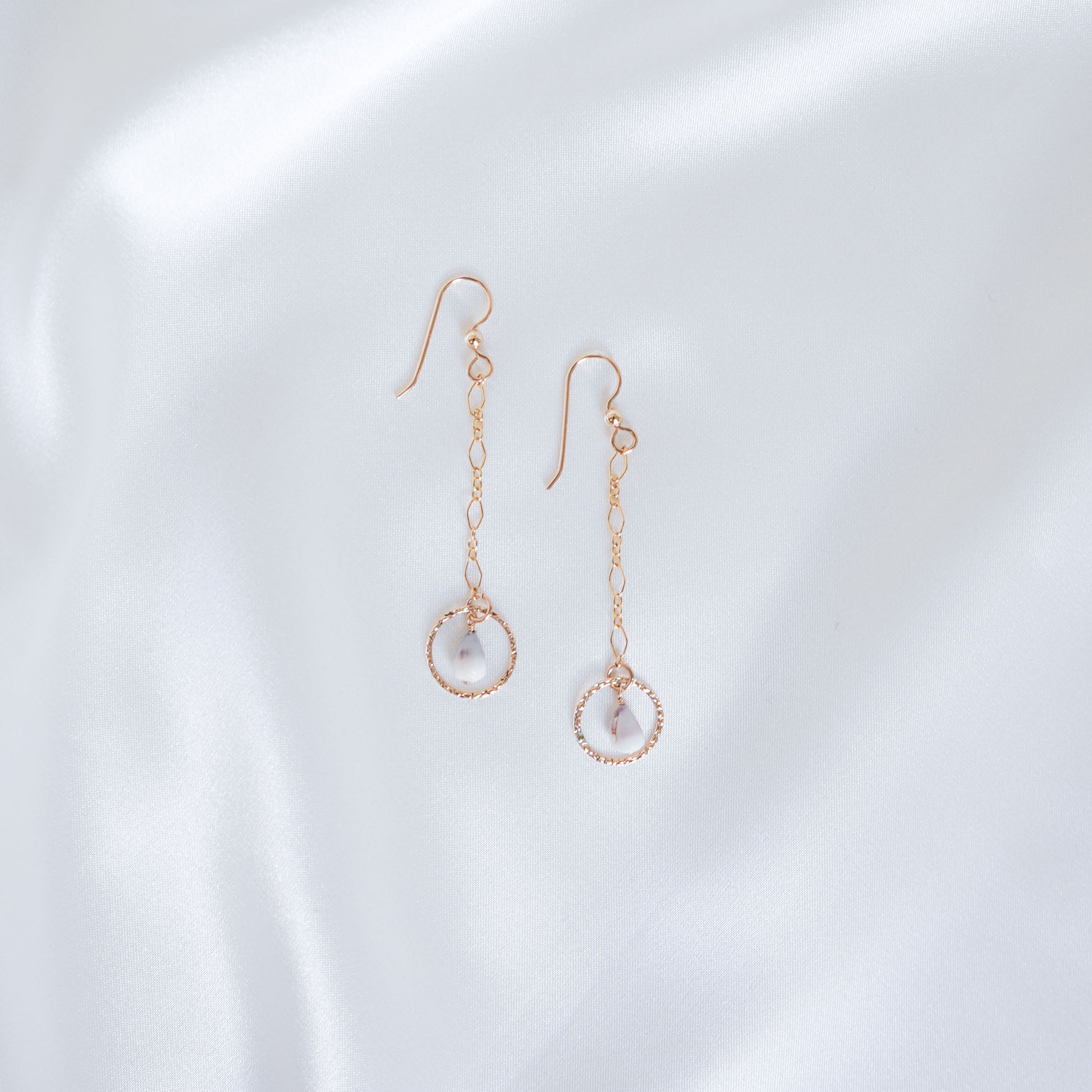 Gold dangle chain earrings with small gold circle and tiny cone shell on a white background