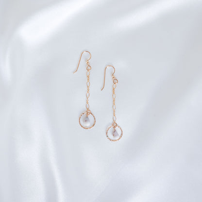 Gold dangle chain earrings with small gold circle and tiny cone shell on a white background