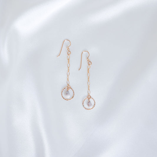 Gold dangle chain earrings with small gold circle and tiny cone shell on a white background
