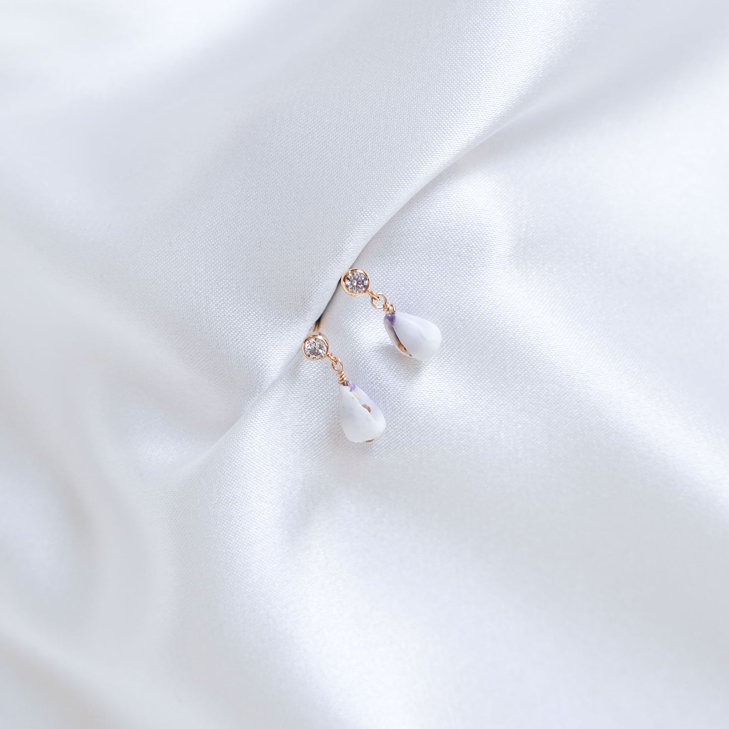 Delicate cz earring stud with tiny white cone shells on white fabric background