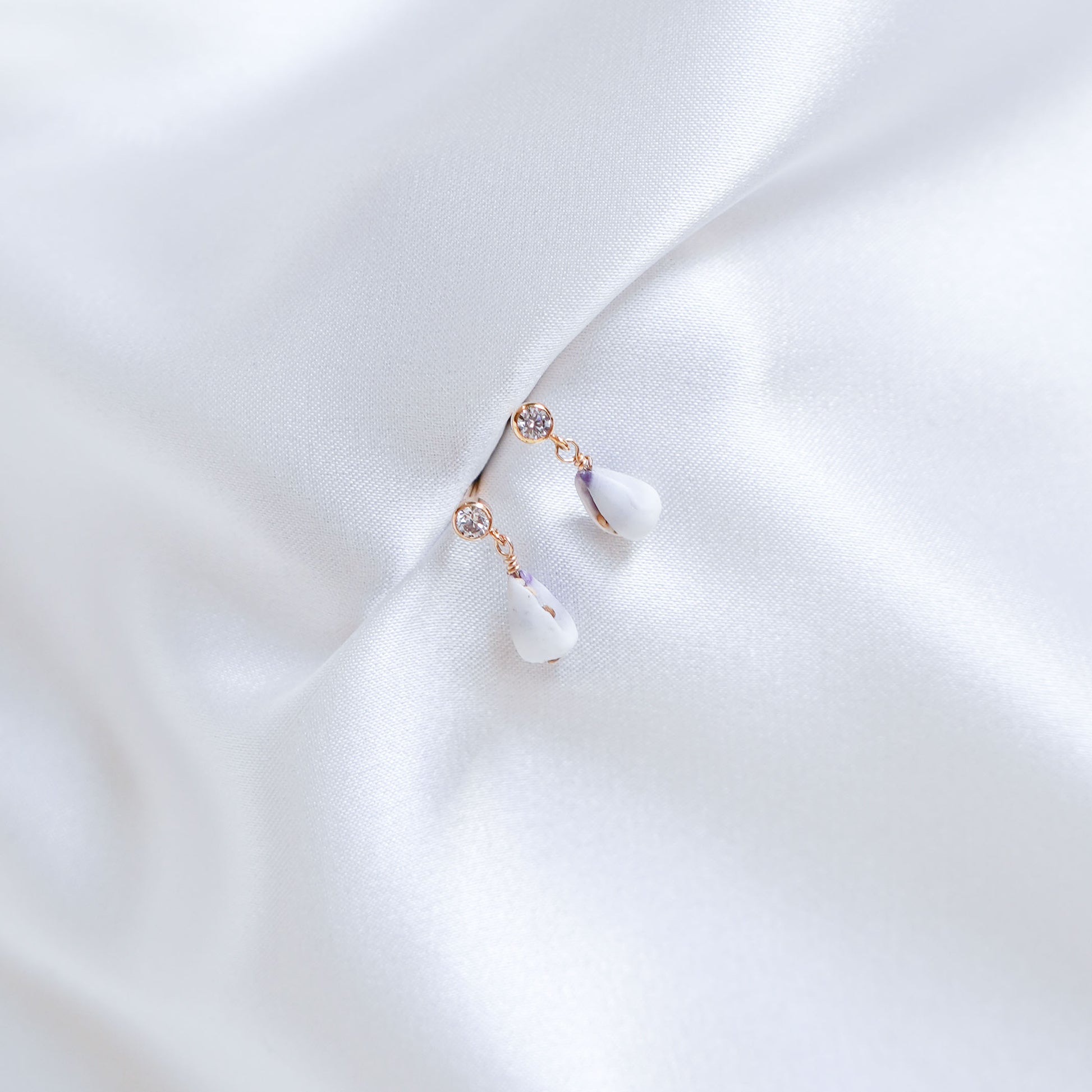 Delicate cz earring stud with tiny white cone shells on white fabric background