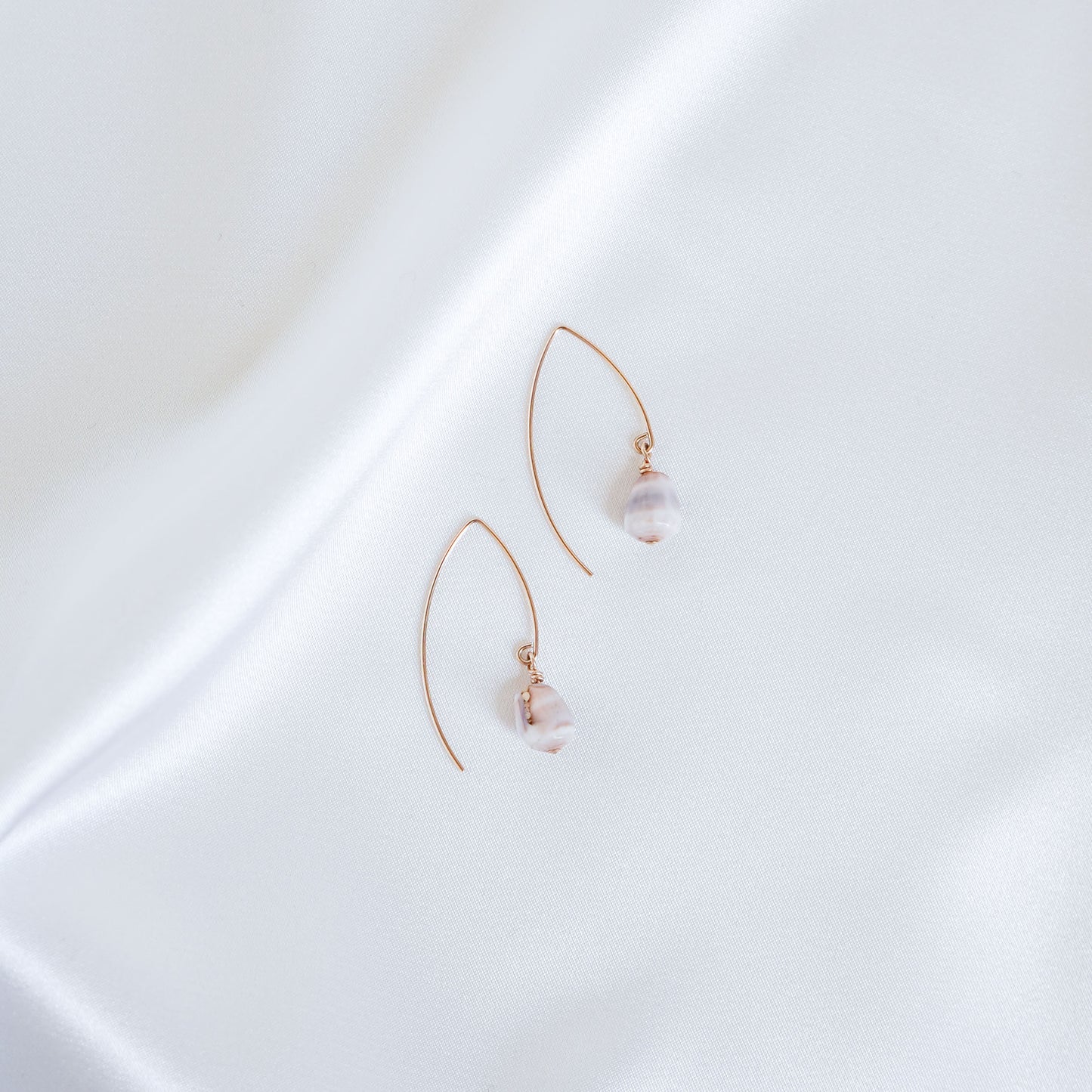 Pair of gold thread hoop earrings with tiny cone shells on a white surface