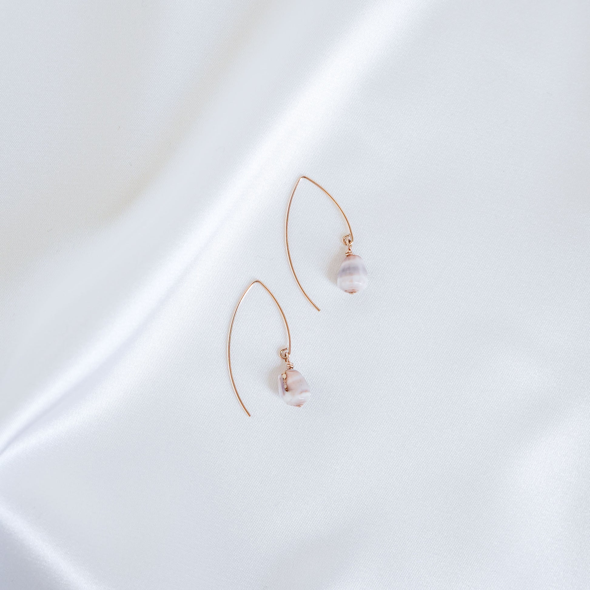 Pair of gold thread hoop earrings with tiny cone shells on a white surface